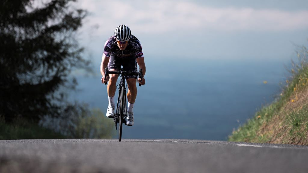 Cyclist pedaling hard uphill on road bike experiencing bottom bracket creaking noise