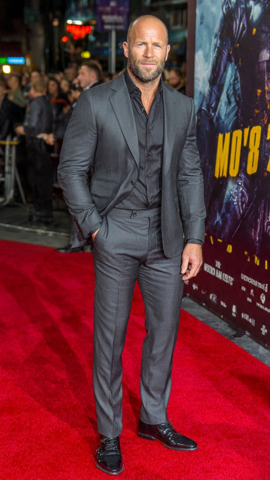 Jason Statham wearing tailored charcoal suit with open collar on red carpet